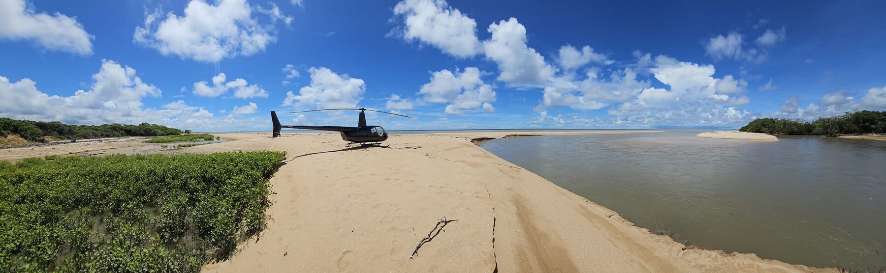 Helicopter parked on a sandbar at a wide Cape York river mouth